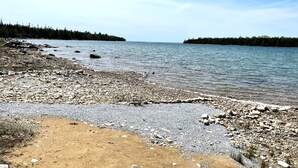 Una costa rocosa con una vista despejada del agua y tierra boscosa a lo lejos.