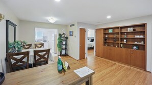 Een ruime woonkamer met een houten eettafel, stoelen, een boekenkast en een deur naar een andere kamer.