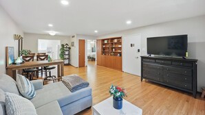 Een ruime woonkamer met een bank, een salontafel, een televisie en een eethoek met stoelen en een tafel.