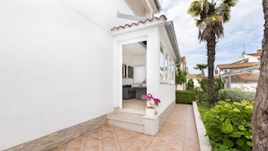Une maison blanche avec une terrasse carrelée et un petit jardin.