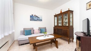 A living room with a sofa, a wooden cabinet, a television, and a painting on the wall. - MAXI One-Bedroom Apartment 2 (Rovinj)