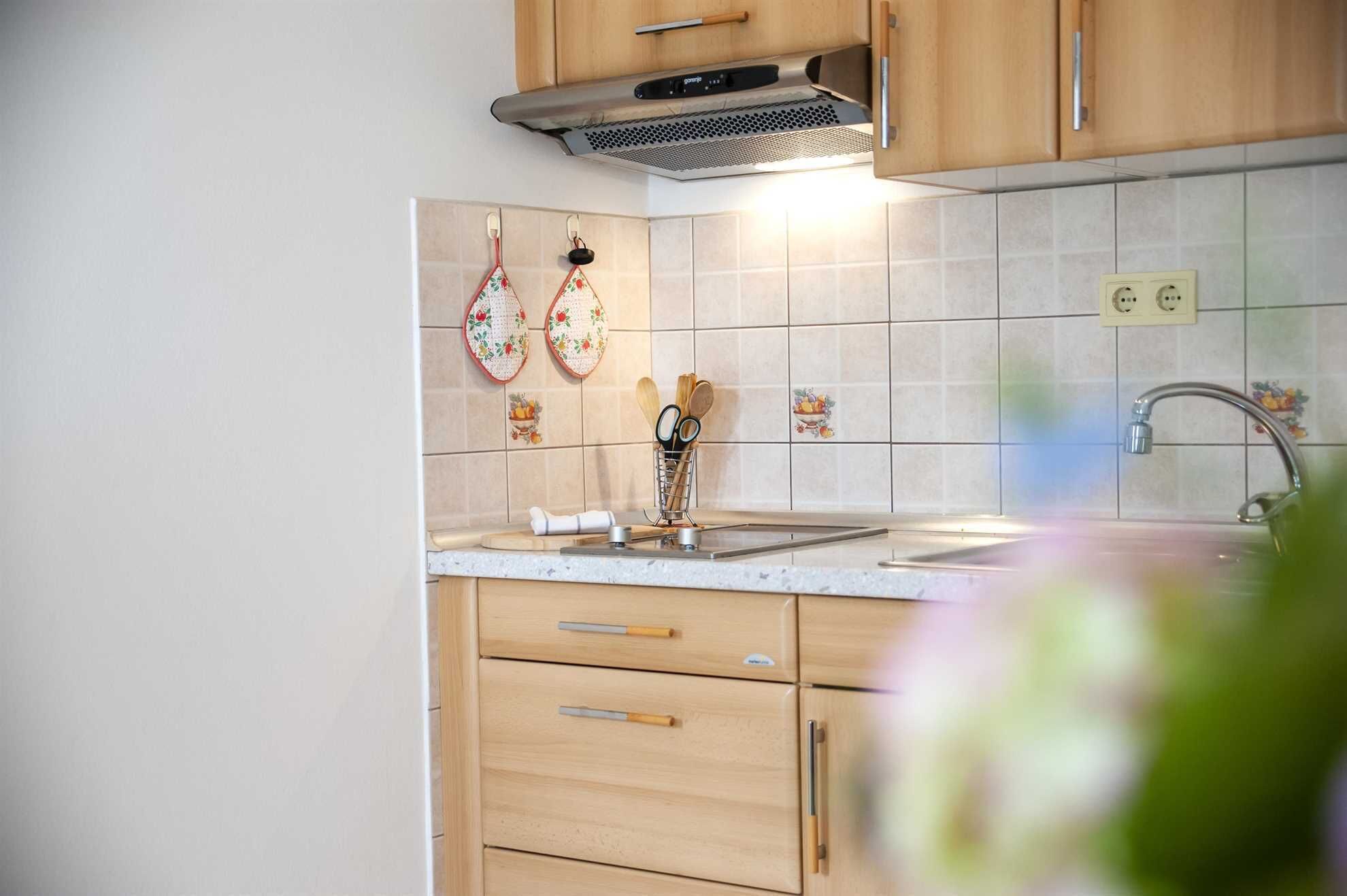 A kitchen with wooden cabinets, a stainless steel range hood, a tiled backsplash, and a sink with a faucet.