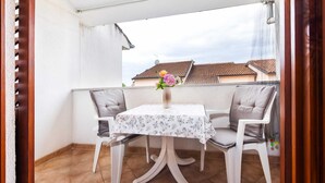 A balcony with a table and two chairs, a vase with flowers, and a view of buildings in the background.