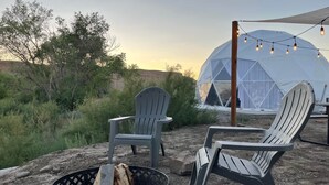 A geodesic dome tent with string lights, two Adirondack chairs, and a fire pit with logs. - Capitol Reef Dome | Oak (Wayne County)