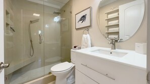 Une salle de bain moderne avec une douche à parois de verre, un lavabo blanc avec un miroir et un tableau encadré représentant une tortue de mer.