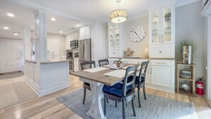 A modern kitchen with white cabinetry, a central island, and a dining area with a table and chairs. - 804 Clipper Court at The Sea Pines Resort (Hilton Head Island)