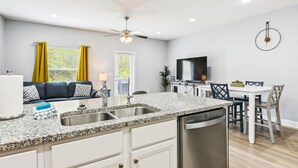 Cozinha moderna com bancadas de granito, lava-louças e uma área de jantar com mesa e cadeiras brancas.