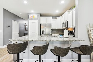 A modern kitchen with white cabinets, a granite countertop, and bar stools. - 7664 Shadow Lake - Happy Horizons - 3 Bedroom 3 Townhouse by RedAwning (Panama City Beach)