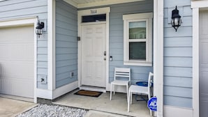 Uma casa com porta de garagem, porta principal, janela e varanda com duas cadeiras e uma mesa pequena.