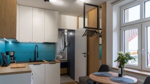 Cocina compacta con un lavabo, cafetera y encimera de madera. Hay una zona de comedor con mesa y sillas, y una ventana con vistas al exterior.