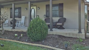 A house with a covered porch, two rocking chairs, a small table, and a potted plant. -  Songbird Haven, 3 min from town, Pumpkinvine, MEC,concerts. 3 bedroom, 2 bath.  (Shipshewana)