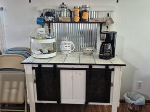 Et tekøkken med kaffemaskine, en kop, en skål og en hylde med kaffedåser.