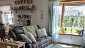 A living room with a leather sofa, a coffee table, and a view of the garden through a window. -  Songbird Haven, 3 min from town, Pumpkinvine, MEC,concerts. 3 bedroom, 2 bath.  (Shipshewana)
