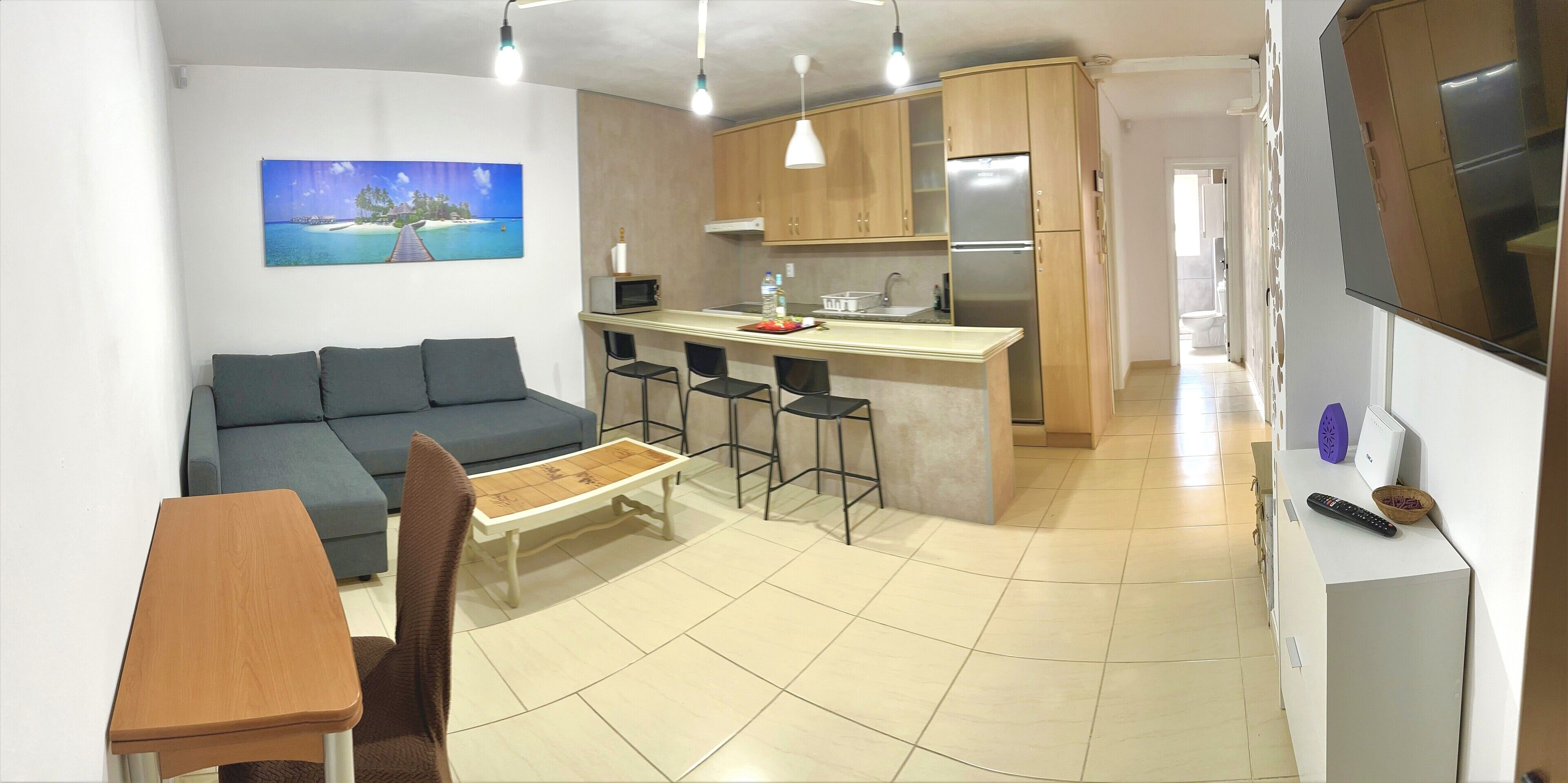 A compact living space with a sofa, dining table, kitchen area, and a TV.