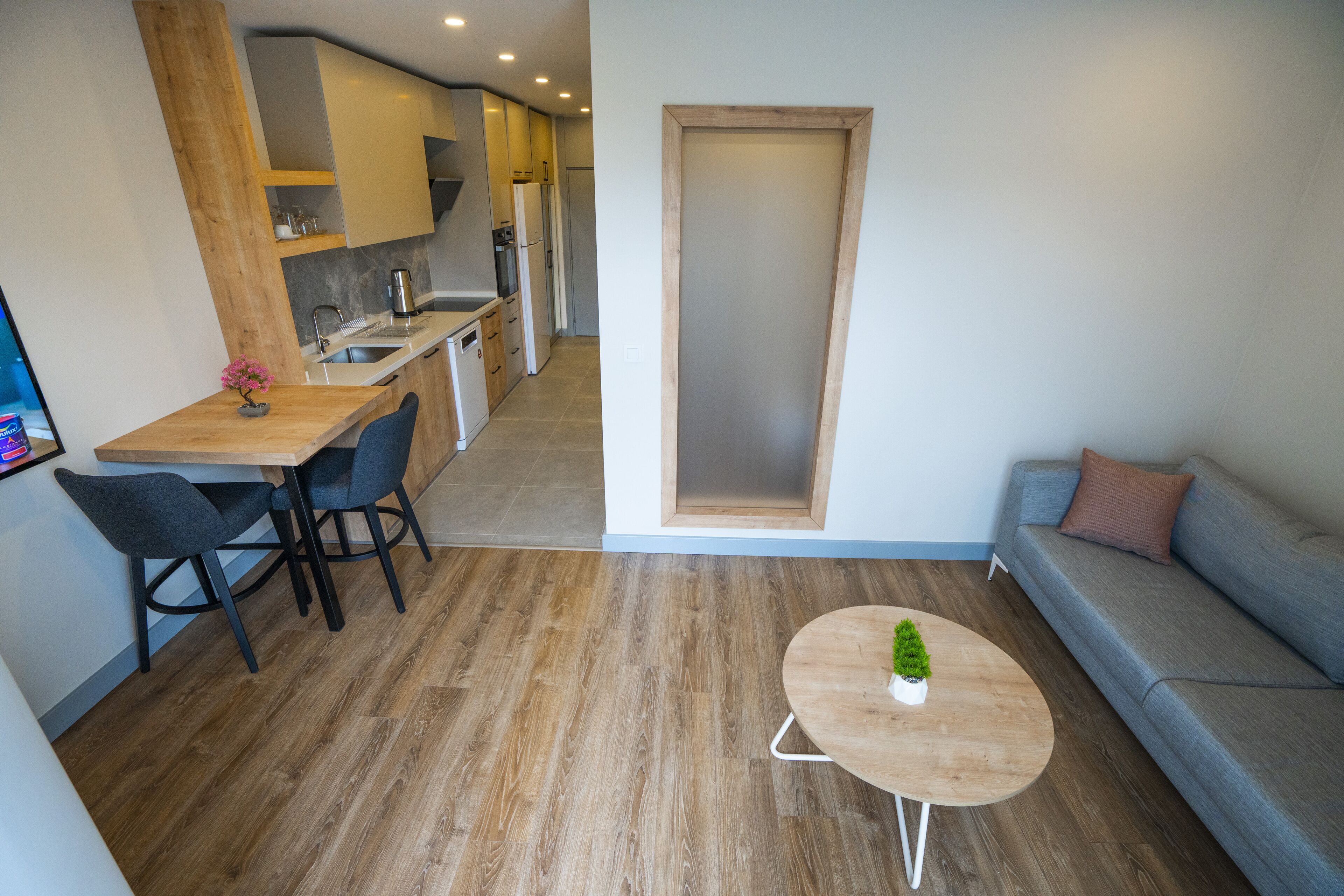 A modern living space with a dining area, a sofa, and a kitchen in the background.