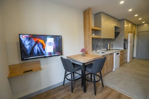 Uma cozinha moderna com uma mesa de jantar de madeira, duas cadeiras, uma TV fixada na parede e armários embutidos.