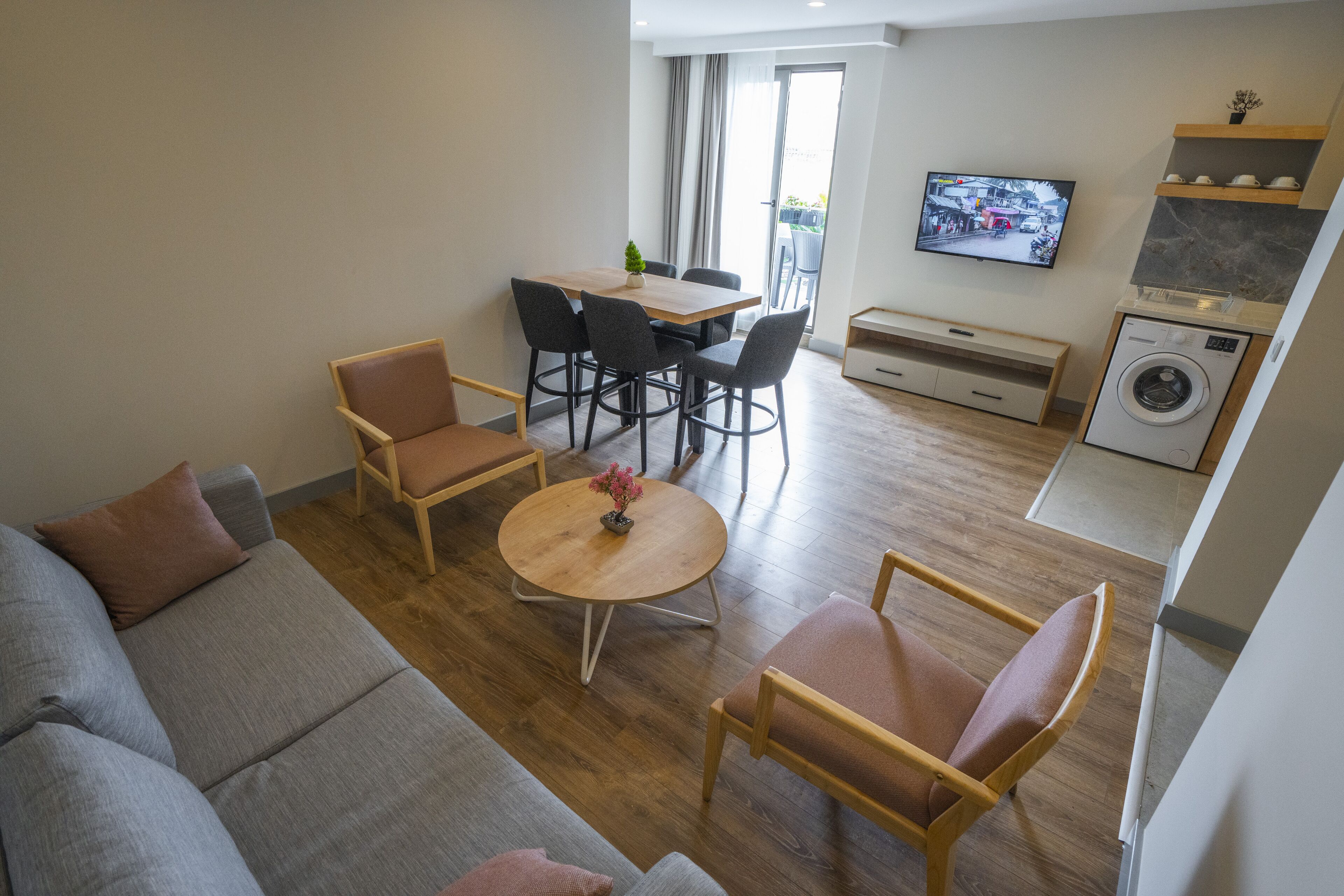 Un salon moderne comprenant un canapé, des fauteuils, une table ronde, un téléviseur et un lave-linge.