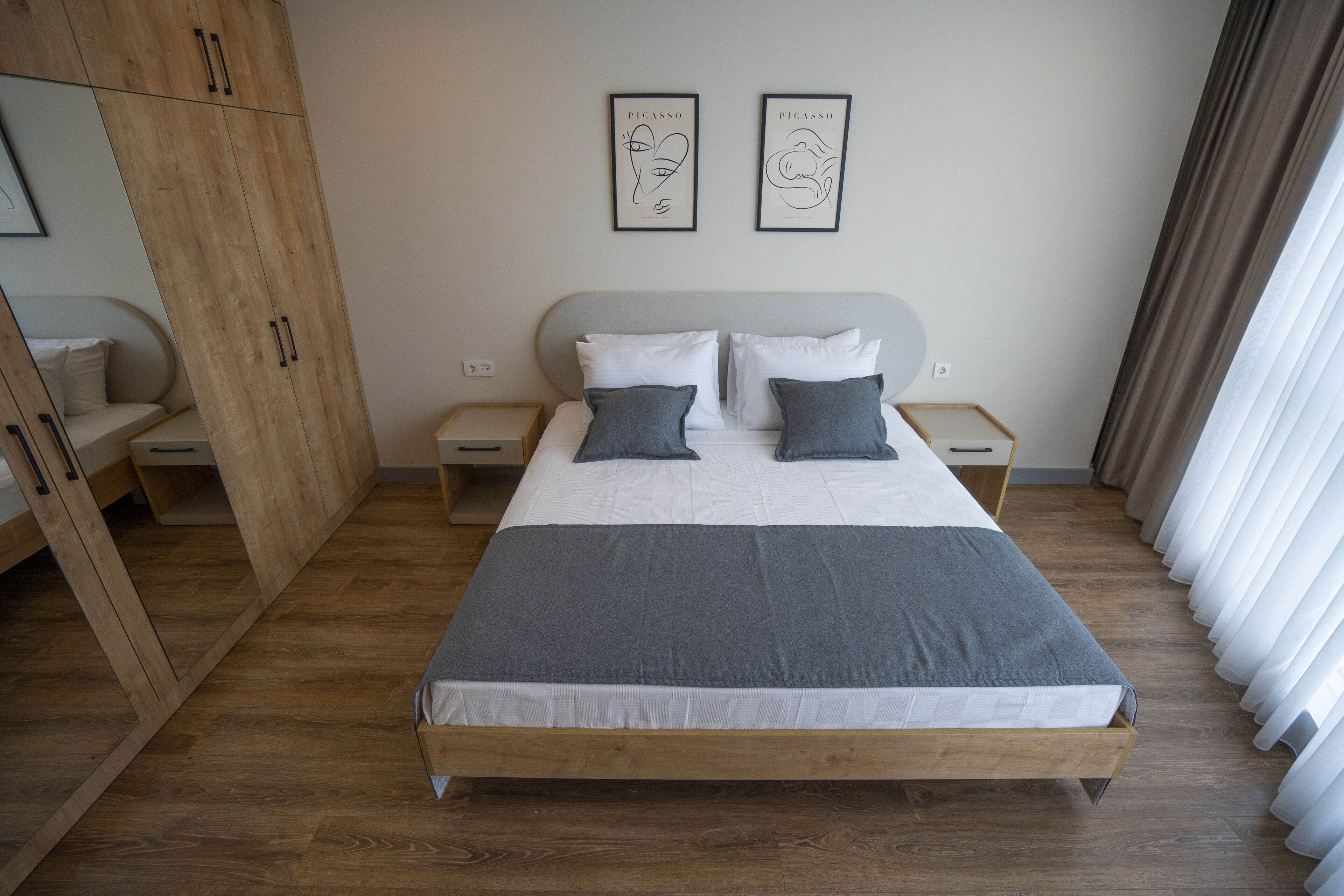 A bedroom with a wooden bed, two bedside tables, a wardrobe, and two framed artworks on the wall.