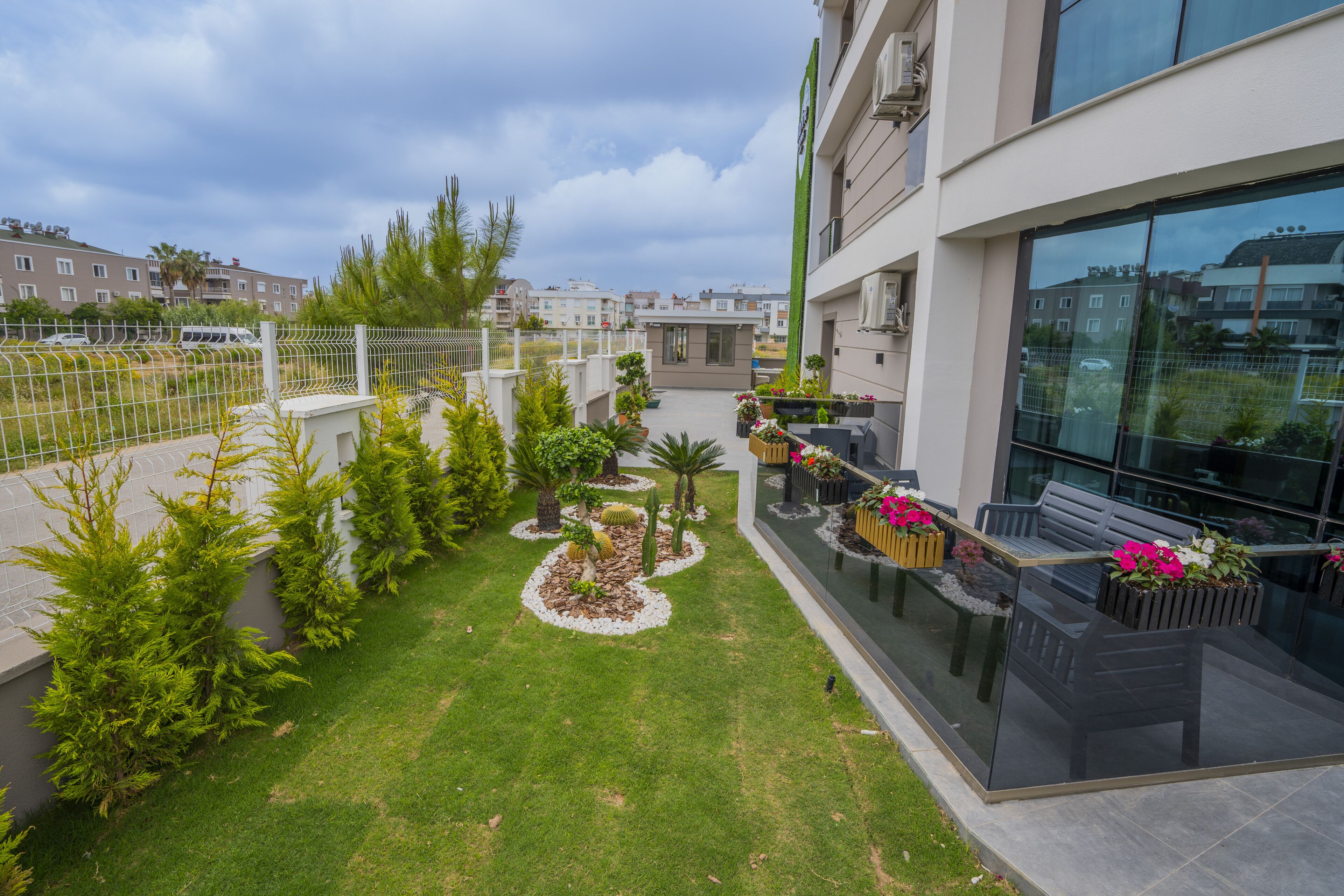 A modern building with a glass facade, a rooftop garden with various plants and a seating area with a bench and table.