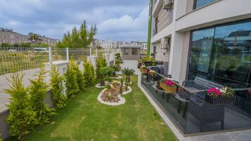 A modern building with a glass facade, a rooftop garden with various plants and a seating area with a bench and table.
