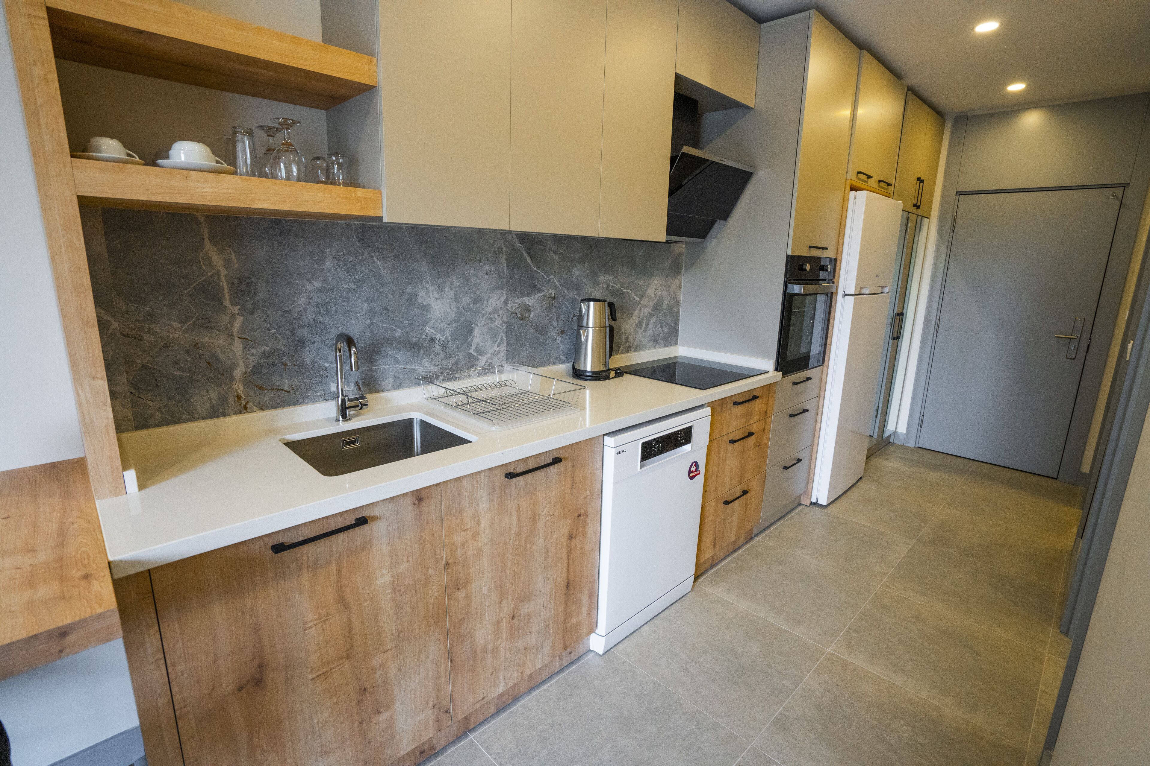 A modern kitchen with wooden cabinets, a white countertop, a built-in dishwasher, and a stainless steel coffee maker.