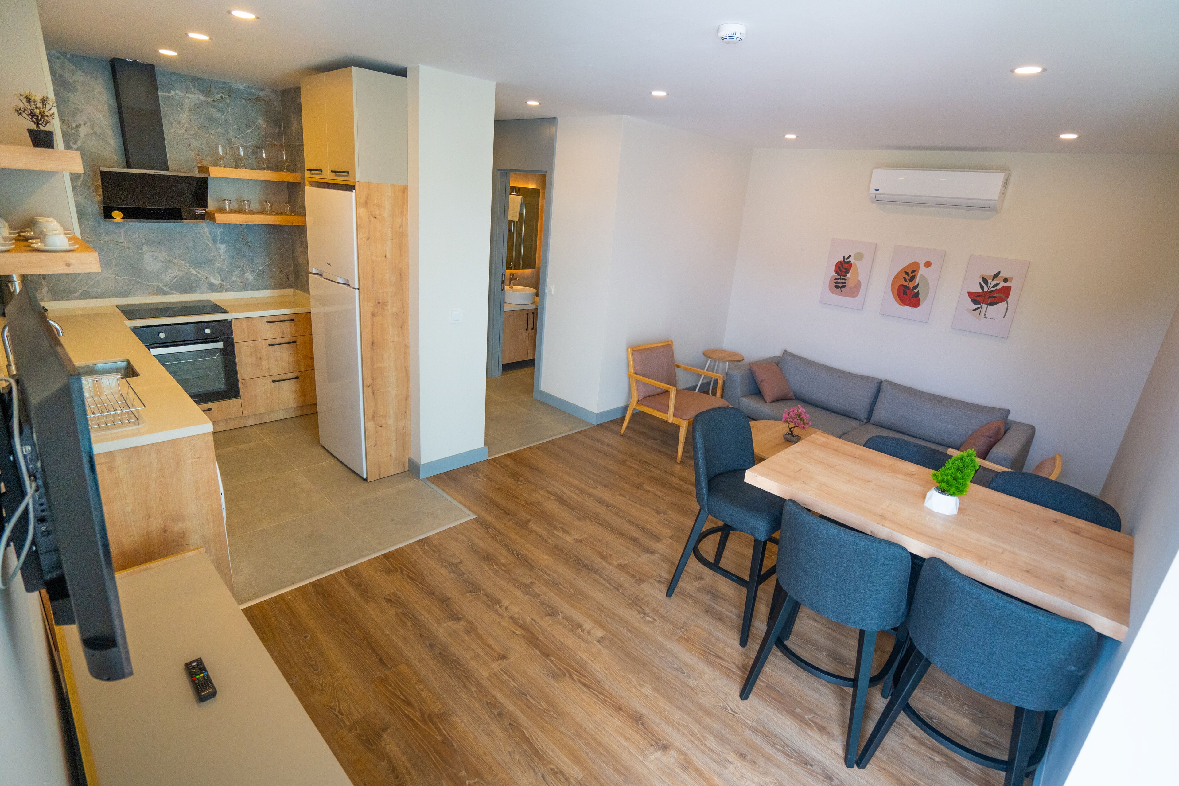A modern kitchen with wooden cabinets, a built-in oven, and a dining area with a wooden table and blue chairs.