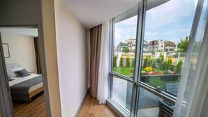 A modern hotel room with a large window, a wooden floor, a bed with grey bedding, and a view of a residential area. - Let'stay Marine Homes (Antalya)