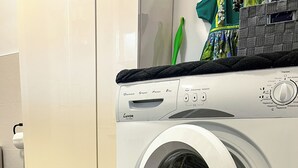 A front-loading washing machine in a laundry room with a wooden floor and a green mat.