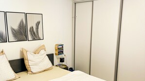 A neatly made bed with a white duvet and pillows, a bedside table with a lamp, and a wardrobe with a mirror.