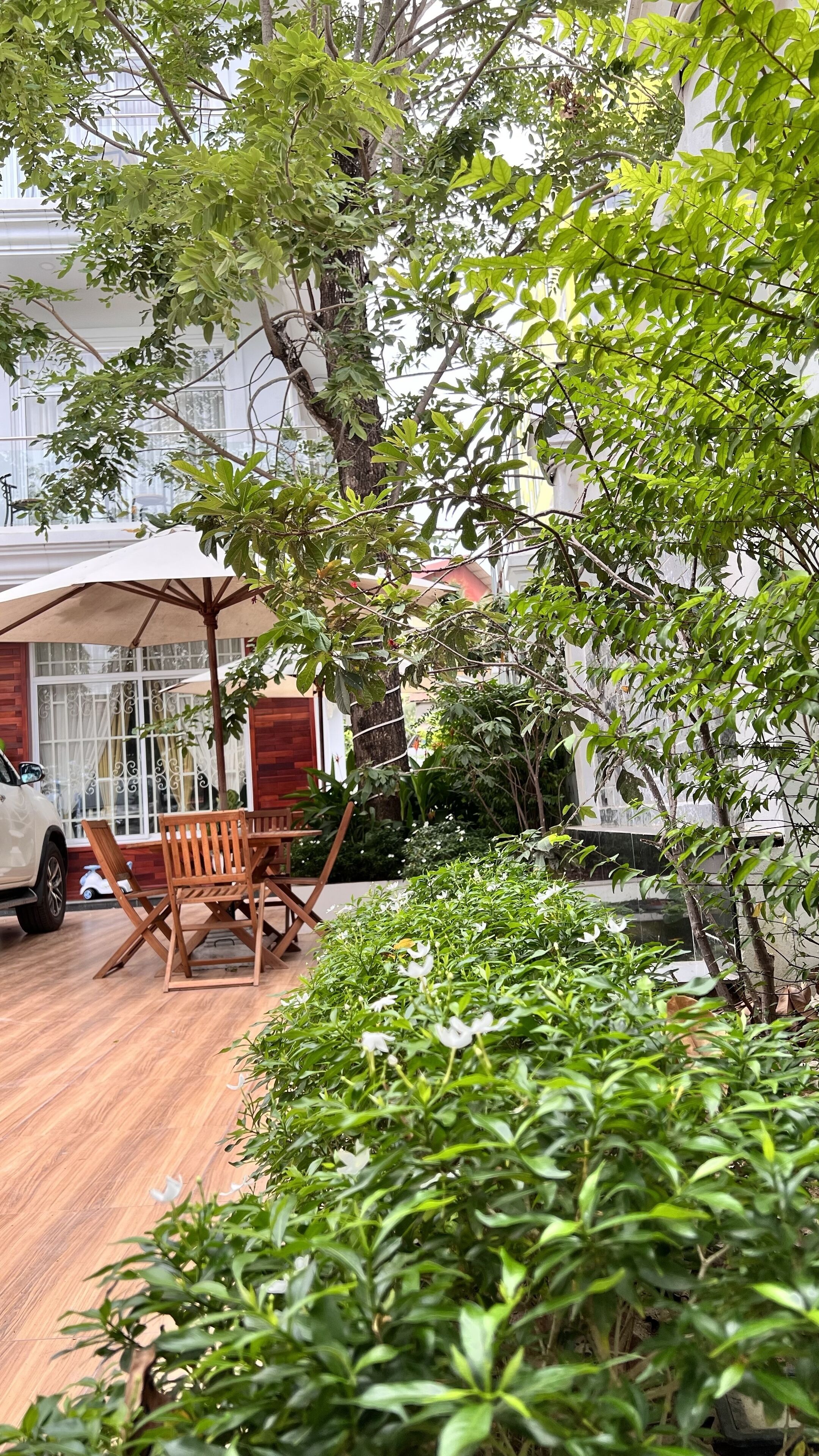 Eine Holzterrasse mit Gartenmöbeln, umgeben von üppiger Vegetation und einem weißen Auto in der Nähe.