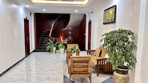 A spacious lobby with a marble floor, a wooden staircase, and a seating area with a large potted plant.