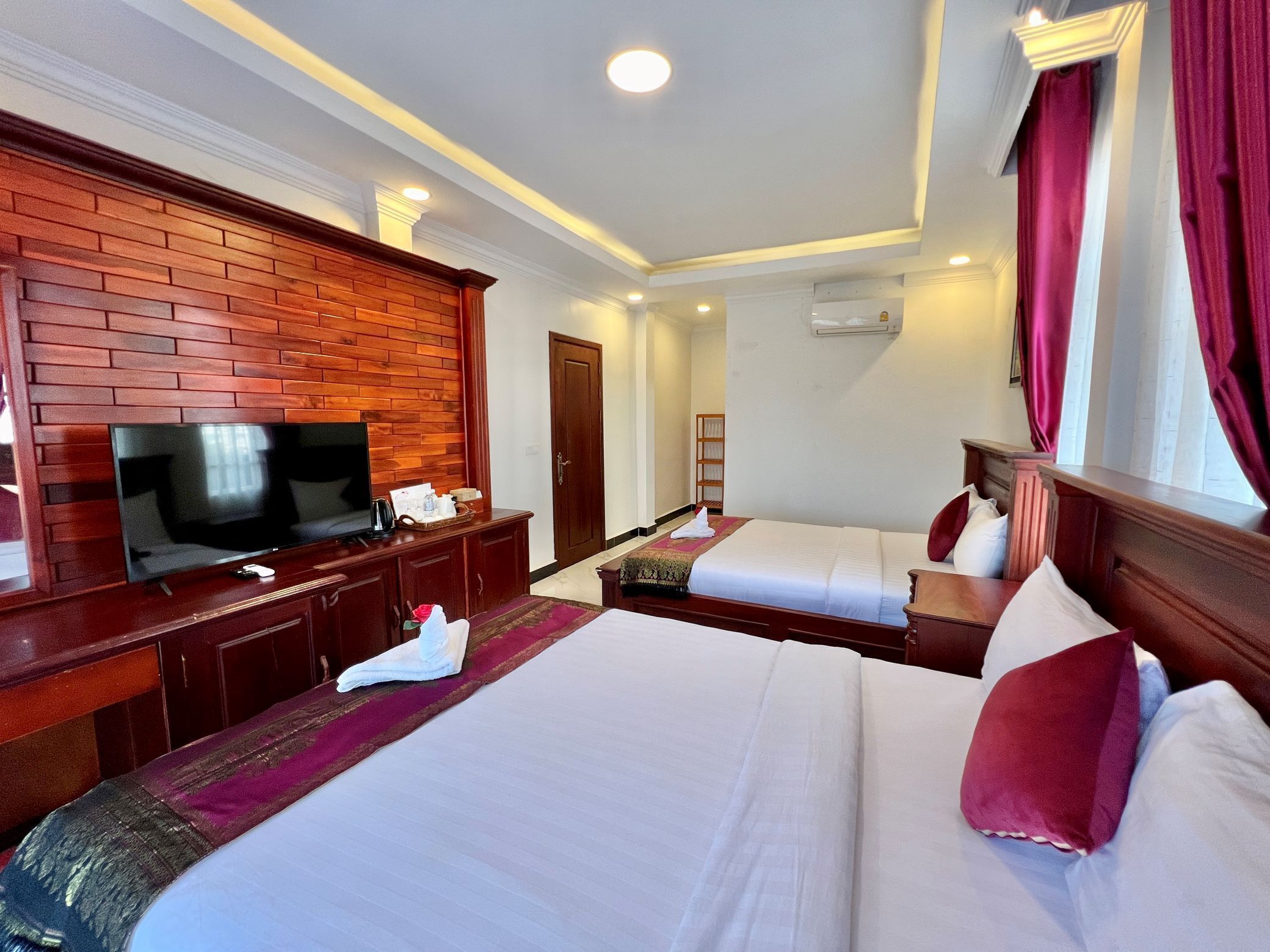 Habitación de hotel con pared de ladrillo decorativa, televisor de pantalla plana, dos camas con ropa blanca y cabeceros de madera.