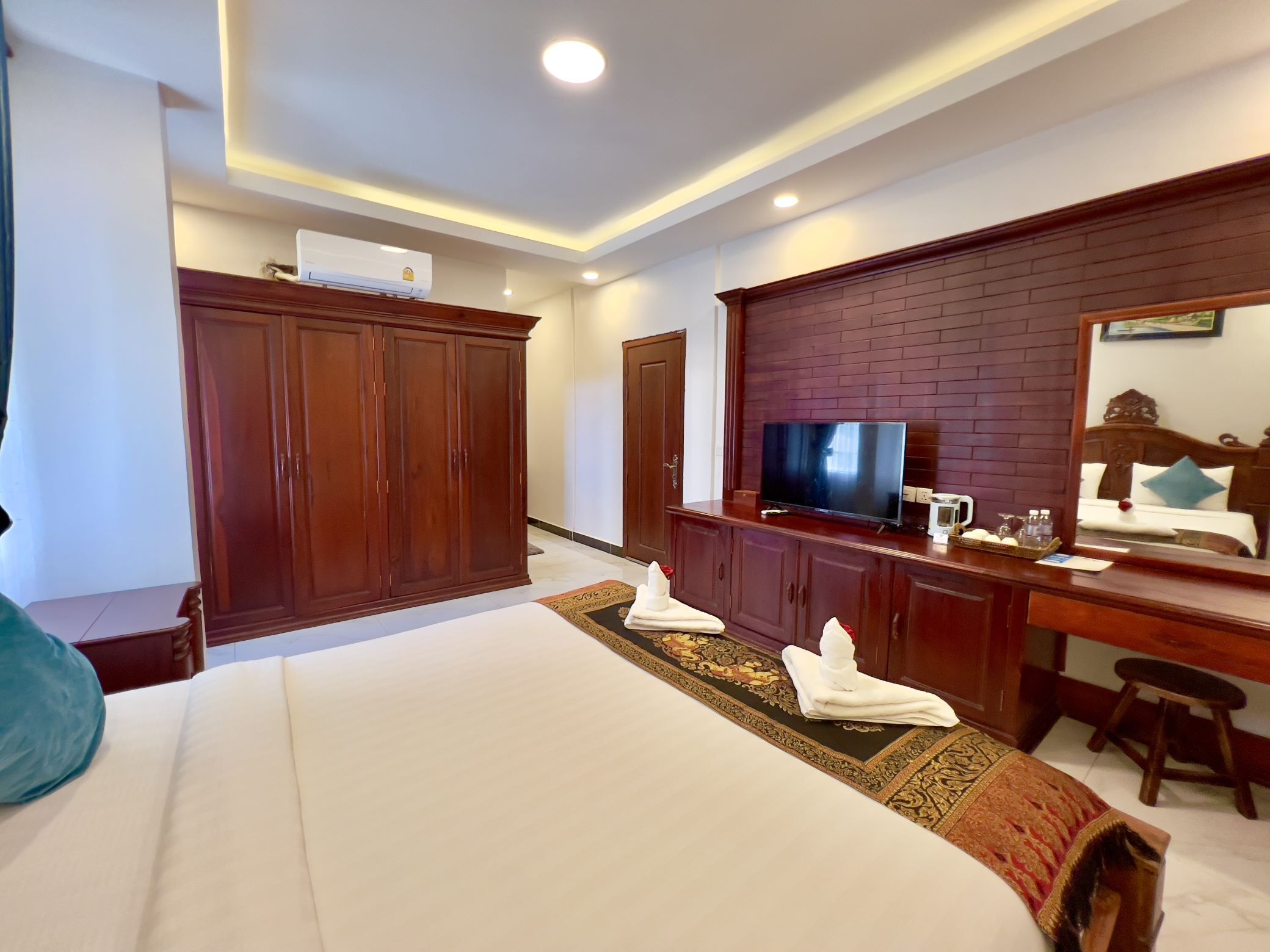 Une chambre d’hôtel avec un grand lit, une armoire en bois, un téléviseur posé sur une commode en bois et un miroir au mur.