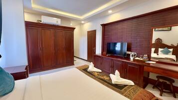 Une chambre d’hôtel avec un grand lit, une armoire en bois, un téléviseur posé sur une commode en bois et un miroir au mur.
