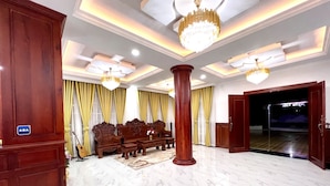 A spacious lobby with marble flooring, ornate wooden furniture, and a grand chandelier.
