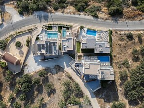 Vista aérea de um resort moderno com várias piscinas, área externa coberta e uma estrada sinuosa nas proximidades.