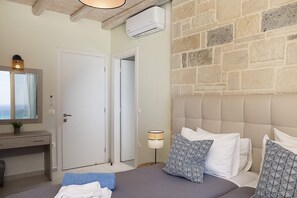 Um quarto com cama, abajur, ar condicionado na parede, porta e janela com cortinas.