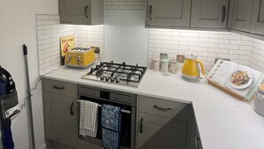 Een compacte keuken met grijze kastjes, een gasfornuis, een gele toaster en een waterkoker op het aanrecht.