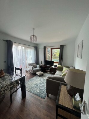 A modern living room with a sofa, a coffee table, a TV, and a dining area with a table and chairs. - Inviting & Spacious 3BD Flat - Shadwell (London)