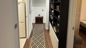 Een gang met een kamerbreed tapijt, een zwart wandrek en een deur naar een kamer met een bed.