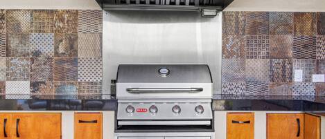 A stainless steel grill with a digital display, wooden cabinets, and a patterned backsplash.