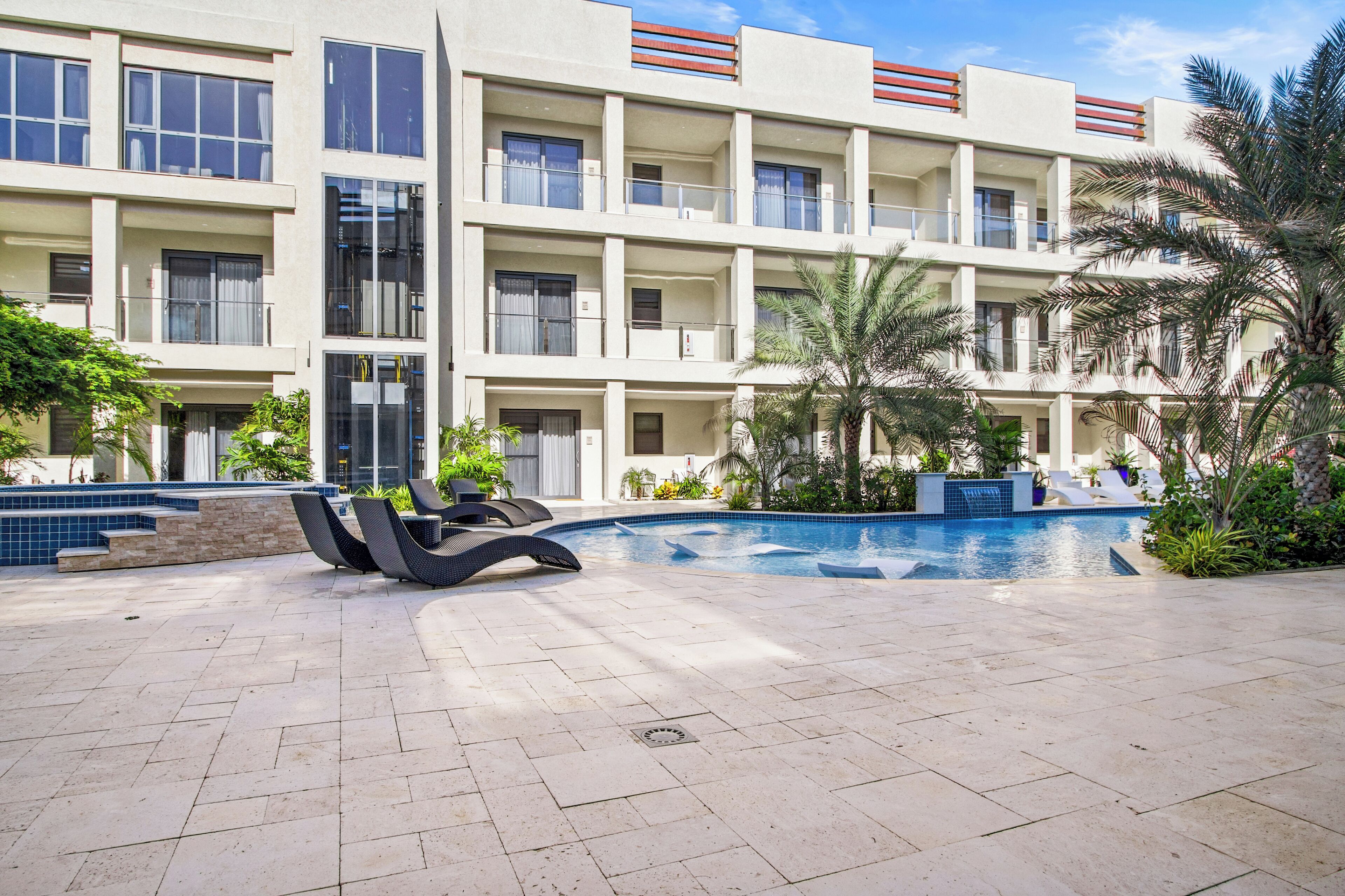 A modern hotel with a pool area, outdoor seating, and a landscaped garden.