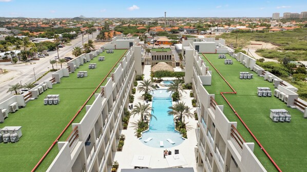 A modern hotel with a central swimming pool, multiple air conditioning units, and a view of the surrounding cityscape. - Wariruri 209 (Noord)