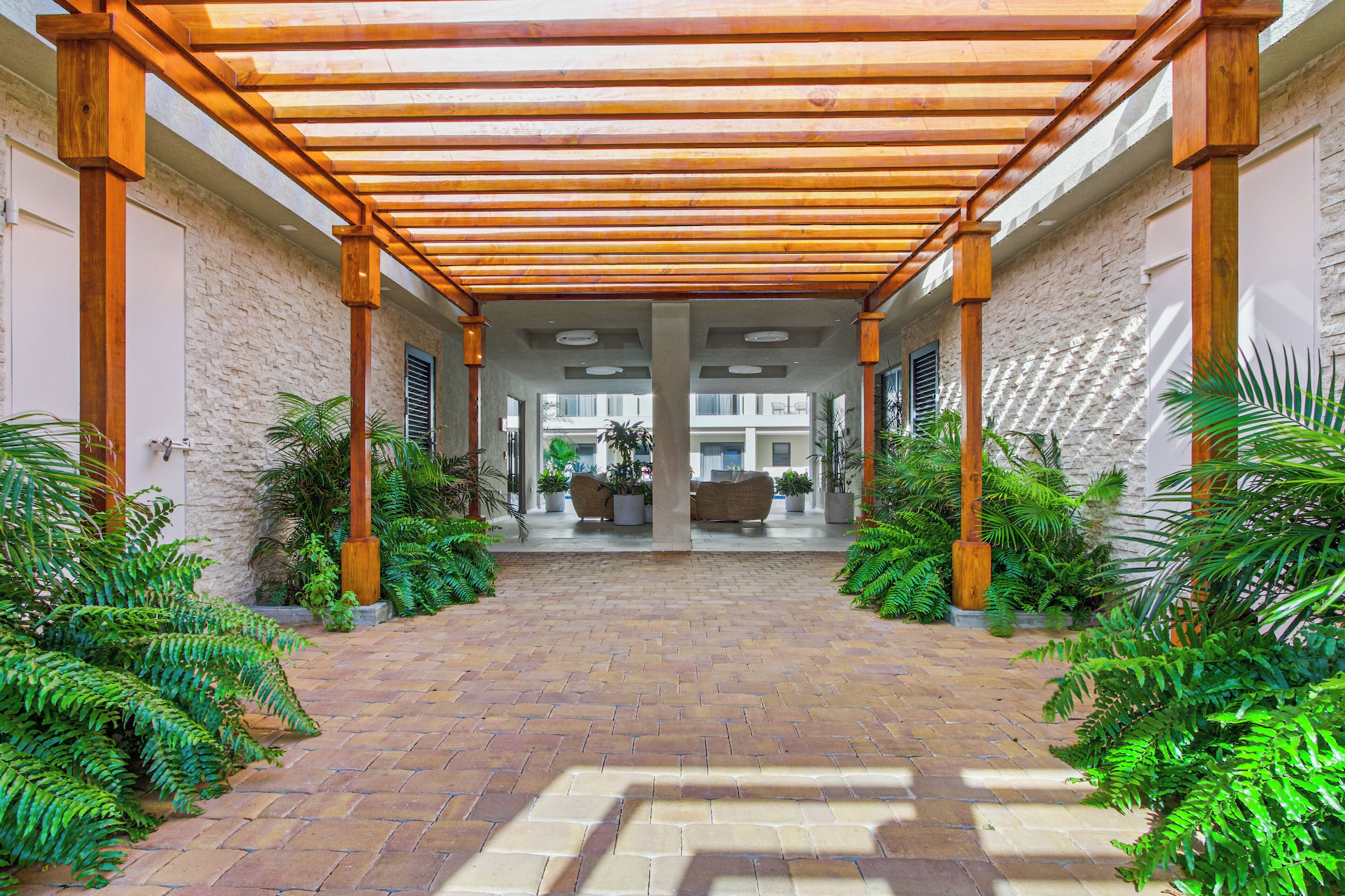 A covered walkway with brick flooring, wooden pillars, and potted plants.