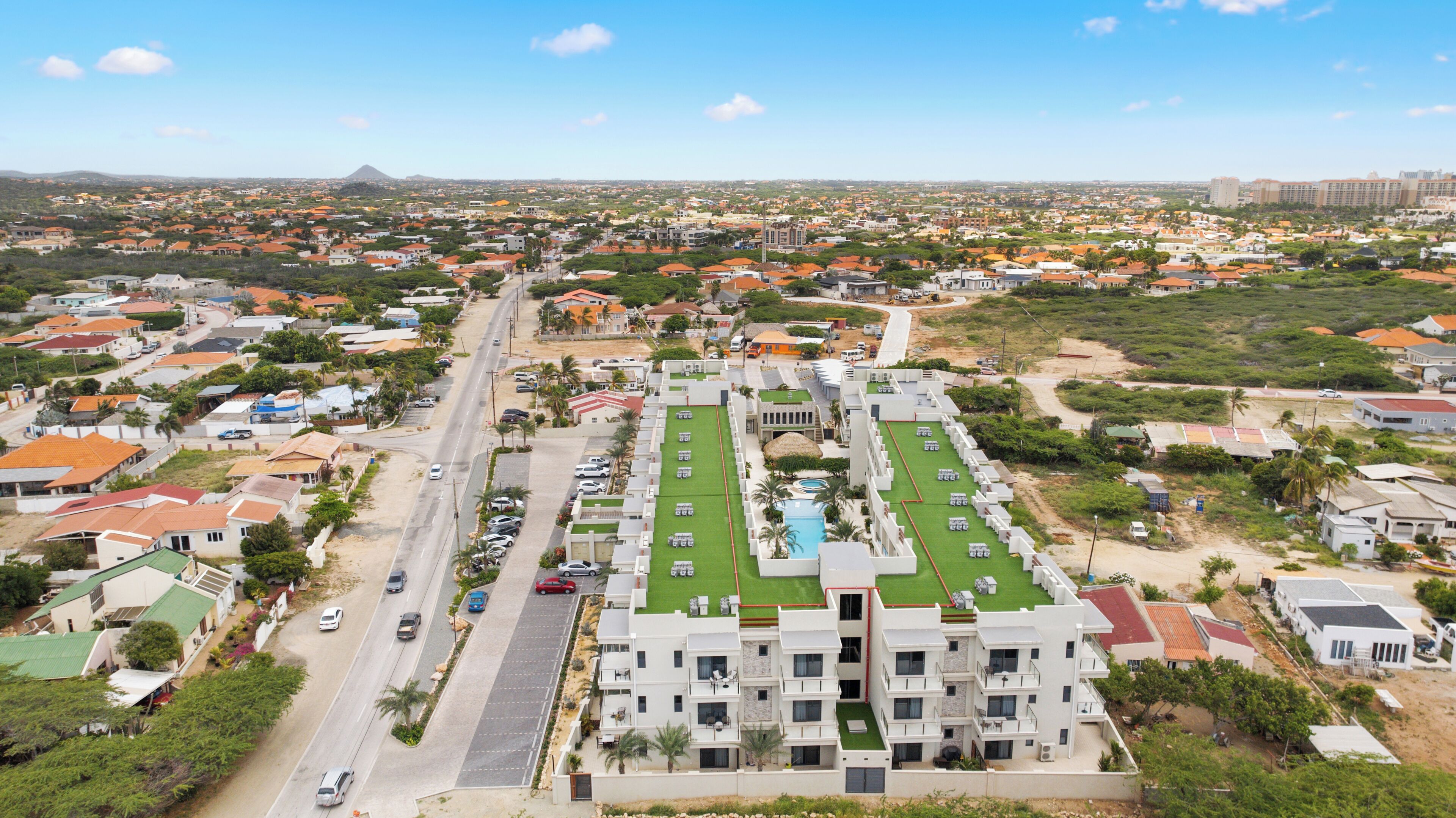 An aerial view of a residential area with a prominent building featuring a rooftop pool and multiple balconies.