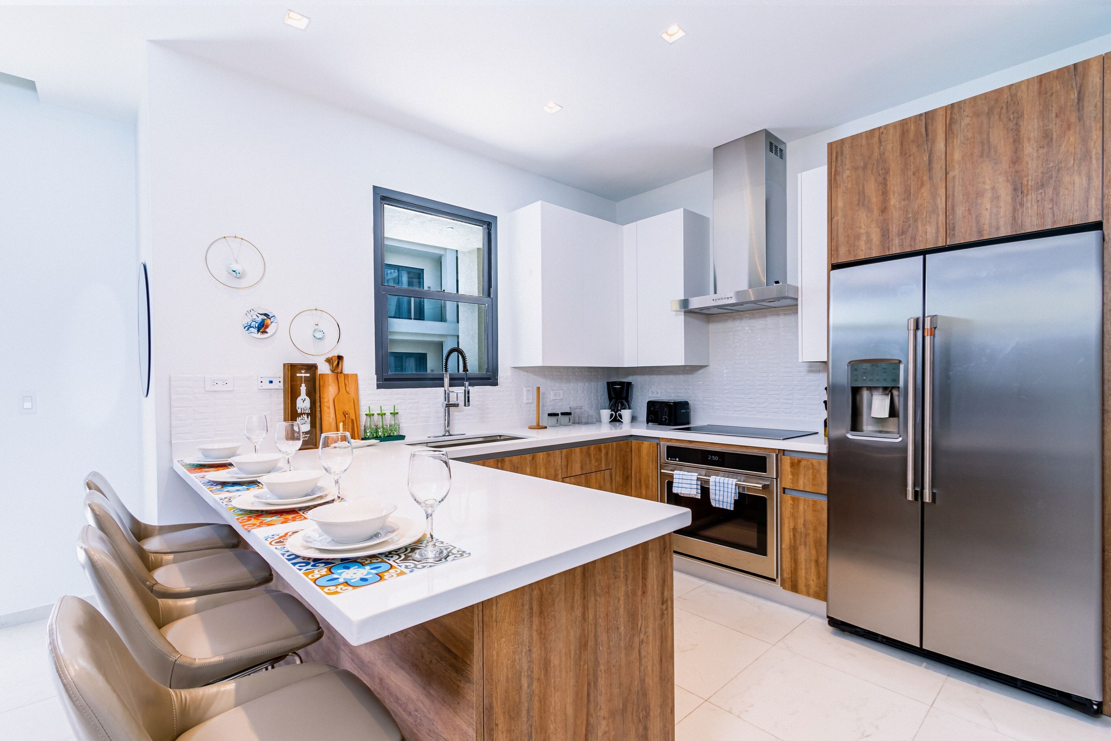 A modern kitchen with a central island, wooden cabinets, stainless steel appliances, and a large window.