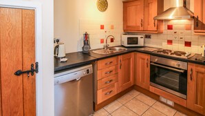 A compact kitchen with wooden cabinets, a stainless steel dishwasher, a microwave, and a stove. - The Coach House At The Gables (Shrewsbury)