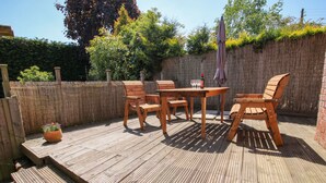 A wooden deck with a table and chairs, surrounded by a bamboo fence and greenery. - The Coach House At The Gables (Shrewsbury)