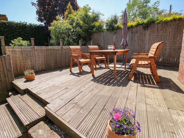 A wooden deck with a table and chairs, surrounded by a bamboo fence and greenery.