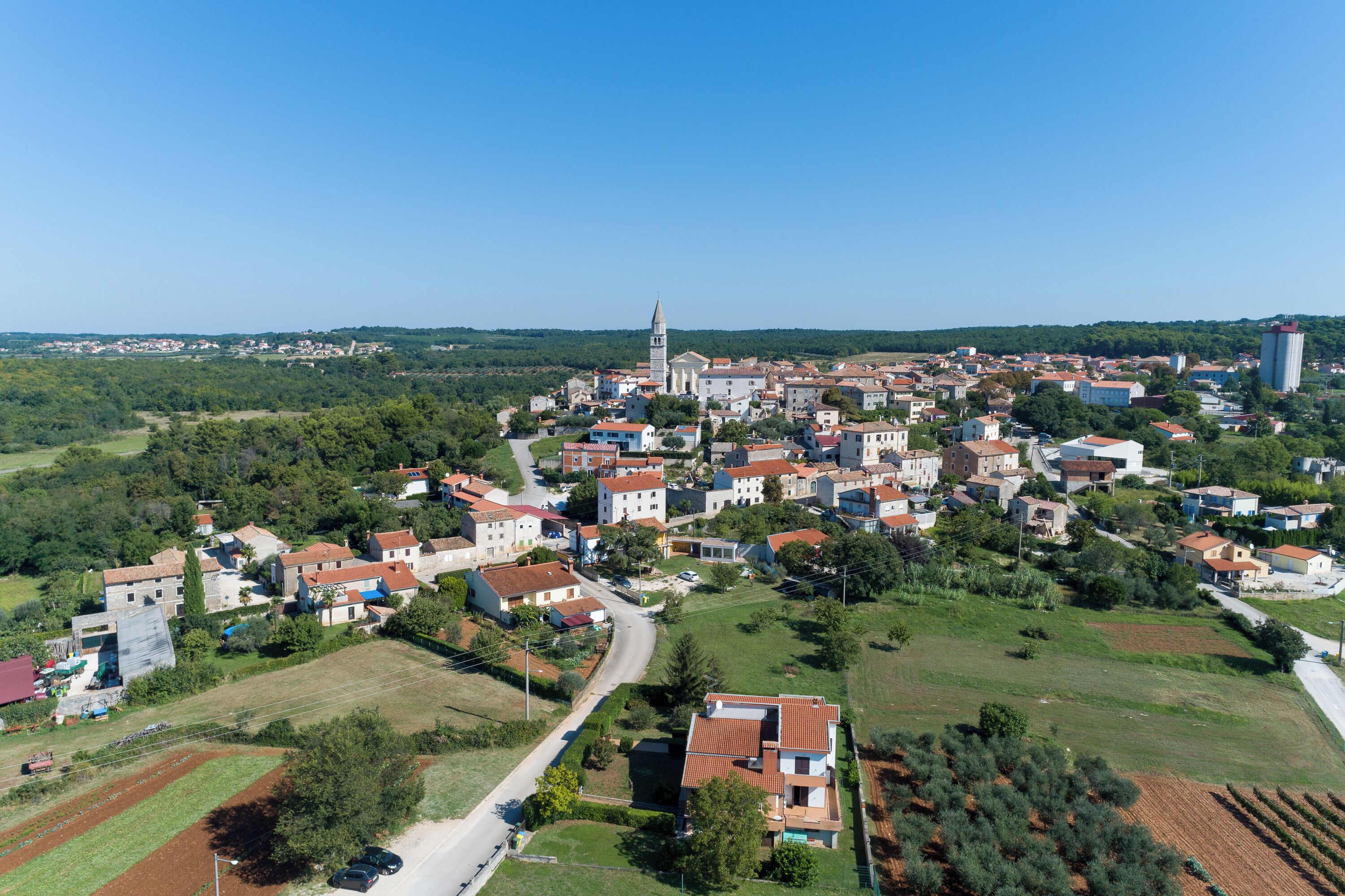 Un pequeño pueblo con una destacada torre de iglesia, rodeado de casas residenciales y campos verdes.